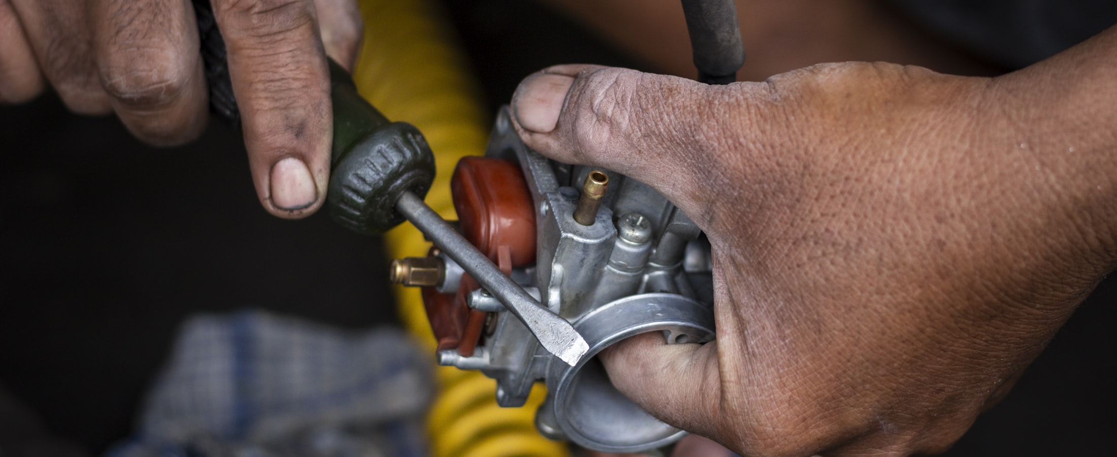 A technician's hands rebuilding a small engine carburettor on the bench